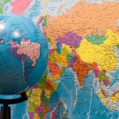 A globe turned to show the Americas is set in front of a wall map displaying Asia