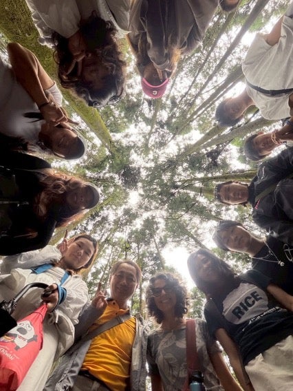 Students in a circle looking down at the camera with trees above them